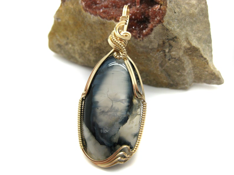 May include: A gold wire wrapped pendant featuring a gray and white agate stone. The stone has a unique pattern of swirls and veins.
