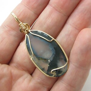 May include: Gold wire wrapped pendant featuring a gray and white agate stone with a unique pattern.