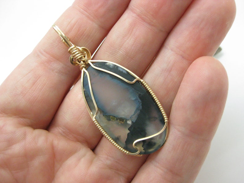 May include: Gold wire wrapped pendant featuring a gray and white agate stone with a unique pattern.