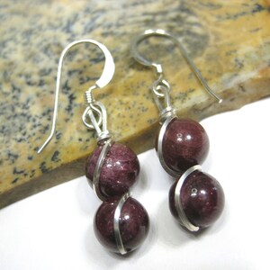 May include: A pair of silver earrings with two dark red gemstone beads on each earring. The beads are wrapped in silver wire.