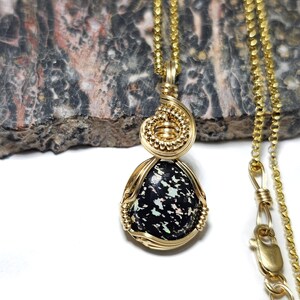 May include: A gold chain necklace with a black and white opal pendant wrapped in gold wire.