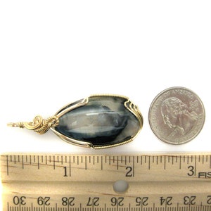 May include: A silver and black gemstone pendant wrapped in gold wire. The pendant is approximately 1 inch long and is shown next to a US quarter for size comparison.