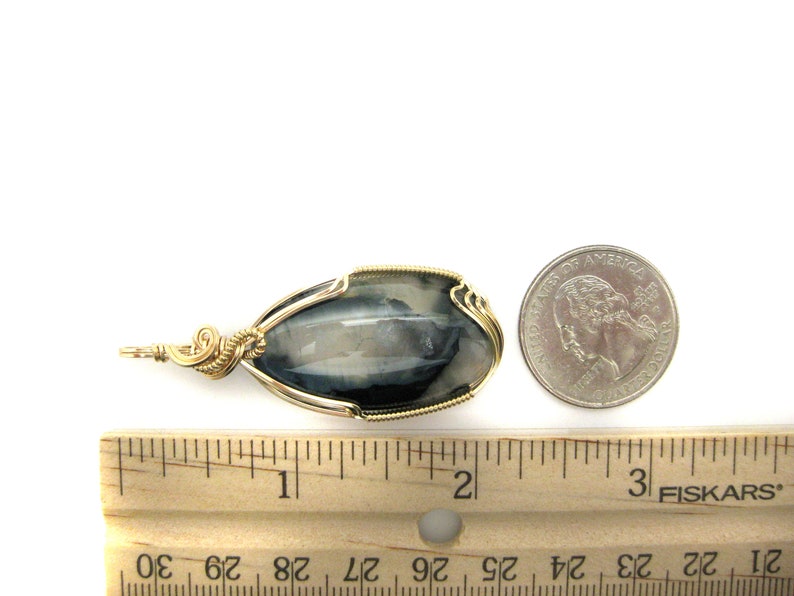 May include: A silver and black gemstone pendant wrapped in gold wire. The pendant is approximately 1 inch long and is shown next to a US quarter for size comparison.