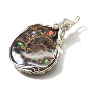 May include: A teardrop-shaped pendant featuring an iridescent ammonite fossil encased in a silver wire wrap. The fossil displays a spiral pattern with colorful, shimmering chambers. The pendant has a silver bail for hanging.