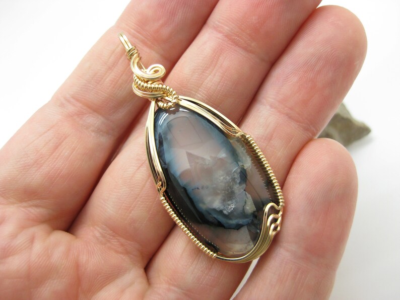May include: Gold wire wrapped pendant featuring a gray and white agate gemstone with a unique pattern.