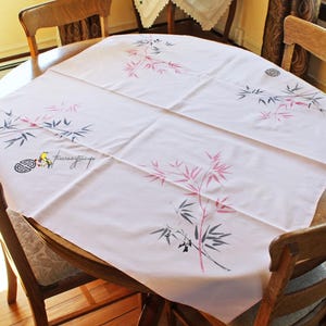 May include: A pink tablecloth with a black and pink bamboo design. The tablecloth is on a round wooden table with two wooden chairs.