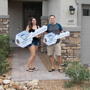 The photo is a man and woman holding signs. The signs say "WE JUST CLOSED ON OUR HOME!" and "SocialCutouts com @socialcutouts".