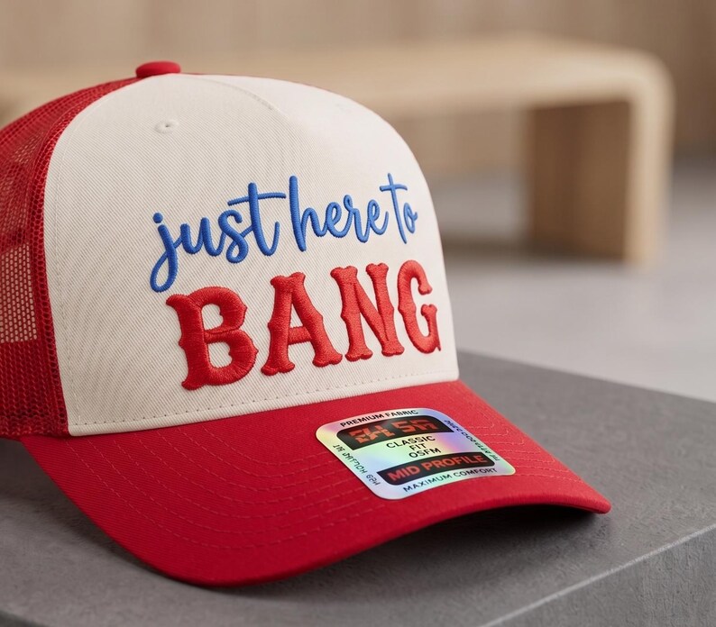 May include: A red and white trucker hat with the text "just here to BANG" embroidered in blue and red. The hat has a red brim and mesh back, and a small red button on top.