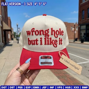 May include: A cream-colored baseball cap with a red brim and red embroidered text that reads "wrong hole but i like it". The cap features a silver Otto brand sticker on the brim and a tan cardboard tag labeled "LittleLoomDigital".