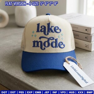 May include: A blue and beige trucker hat with the words "lake mode" embroidered in blue. The hat has a mesh back and a blue brim. A tag with the text "LittleLoomDigital" hangs from the brim.
