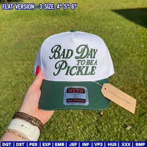 May include: A white and green baseball cap with the text "Bad Day to be a Pickle" embroidered on the front. The cap has a green brim and a tag that says "LittleLoomDigital".
