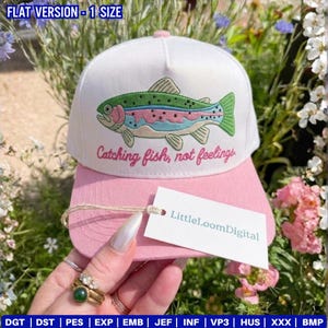 May include: A white and pink baseball cap with an embroidered rainbow trout design. The cap features the text "Catching fish, not feelings." A tag with the text "LittleLoomDigital" is attached.