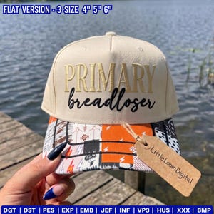 May include: A cream-coloured baseball cap with the text PRIMARY in gold embroidery and breadloser in black script. The brim features a multi-patterned design with orange, white, and black elements. A brown paper tag reads LittleLoomDigital.