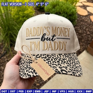 Könnte beinhalten: Eine cremefarbene Baseballkappe mit einem Schirm im Leopardenmuster und goldener Stickerei mit dem Text DADDY'S MONEY but I'M DADDY. Ein braunes, rechteckiges Papieretikett mit der Aufschrift LittleLoomDigital ist mit einer Kordel befestigt.
