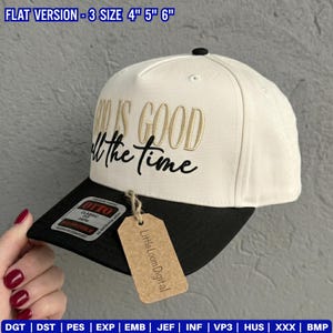 May include: A baseball cap with a cream-colored crown and a black brim. The cap features the embroidered phrase "GOD IS GOOD all the time" in gold and black thread. A small tag with the text "Little Loom Digital" hangs from the brim.