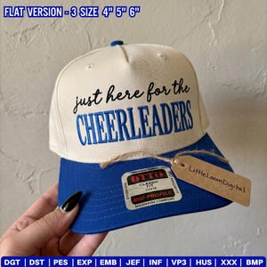 以下が含まれることがあります： 黒と青で「just here for the CHEERLEADERS」と刺繍された、クリーム色のベースボールキャップ。青いツバには「OTTO CLASSIC FIT OSFM MID PROFILE」と書かれたステッカーが貼られ、「LittleLoomDigital」と書かれた茶色のタグが付いています。