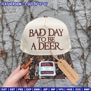 Puede incluir: Una gorra de béisbol color crema con una visera de patrón de camuflaje. El frente presenta un texto bordado en marrón que dice "BAD DAY TO BE A DEER". Una pegatina rectangular en la visera muestra "OTTO" y "CLASSIC FIT", con una etiqueta de papel marrón.