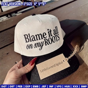 Op de afbeelding: Een wit en zwarte baseball cap met de geborduurde tekst "Blame it all on my ROOTS" in zwart. Een klein label met "LittleLoomDigital" is bevestigd. De pet is een platte versie en is verkrijgbaar in de maten 7,6 cm, 10,2 cm, 12,7 cm en 15,2 cm.
