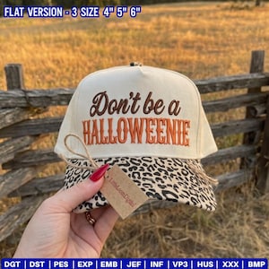Puede incluir: Una gorra de béisbol color crema con visera de estampado de leopardo. El frente presenta el texto bordado en marrón y naranja "Don't be a HALLOWEENIE". Una pequeña etiqueta marrón con la inscripción "LittleLoomDigital" está unida a la visera.