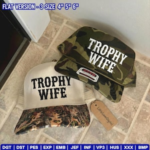 May include: Two trucker hats with the text "TROPHY WIFE" embroidered in white. One hat has a white front and a camouflage brim, the other is camouflage. A small tag reads "Little Loom Digital".