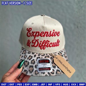 May include: A beige baseball cap with the embroidered words "Expensive & Difficult" in red script. The brim features a leopard print pattern. A tag from "LittleLoomDigital" is attached.