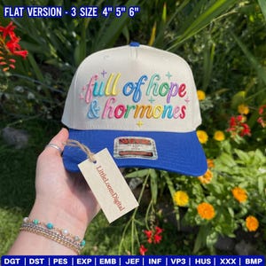 Könnte beinhalten: Eine weiß-blaue Baseballkappe mit dem gestickten Text "full of hope & hormones" in Regenbogenfarben. Die Kappe hat einen flachen Schirm und ein Etikett mit der Aufschrift "LittleLoomDigital".