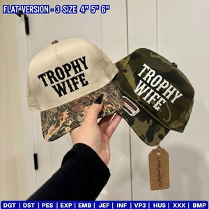May include: Two baseball caps with the text "TROPHY WIFE". One cap has a tan front with a camouflage brim, and the other is camouflage with a green and brown pattern. The caps have a mesh back. The image also includes the text "FLAT VERSION - 3 SIZE 4" 5" 6"".