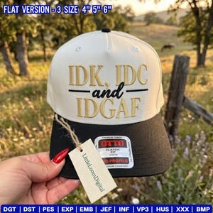May include: A two-tone baseball cap with a white crown and a black brim. The front features gold embroidered text reading IDK, IDC and IDGAF. A rectangular tag with the text LittleLoomDigital hangs from the brim, and an Otto sticker is attached.