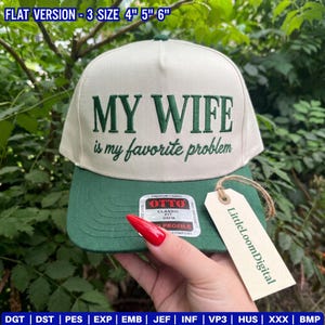 May include: A cream-coloured baseball cap with a dark green brim and embroidered dark green text that reads "MY WIFE is my favourite problem." The cap features an Otto brand sticker on the brim and a beige tag labelled "LittleloomDigital."