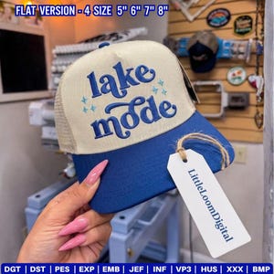 May include: A blue and beige trucker hat with the words "lake mode" embroidered on the front. The hat has a mesh back and a curved brim. The tag reads "LittleLoomDigital".
