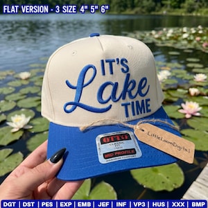 May include: A two-tone baseball cap with a cream-colored crown and a blue brim. The front features blue embroidered text reading IT'S Lake TIME. A rectangular sticker on the brim displays OTTO CLASSIC FIT, and a brown tag reads LittleLoomDigital.