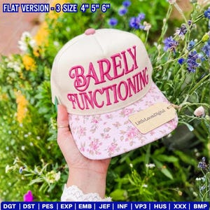 May include: A beige baseball cap with the embroidered phrase "BARELY FUNCTIONING" in pink. The brim features a pink floral pattern. The cap has a pink button on top and a tag that says "LittleLoomDigital".