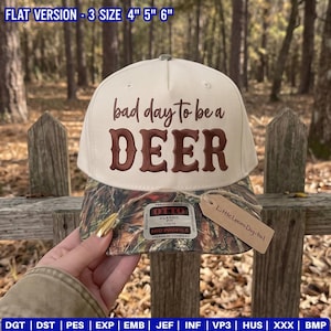 May include: A cream-colored baseball cap with a camouflage brim. The front features the brown text 'bad day to be a DEER'. A sticker on the brim reads 'OTTO CLASSIC' and a brown paper tag attached to the brim reads 'LittleLoomDigital'.