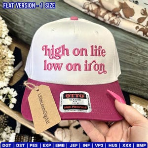 May include: A white and magenta baseball cap with the text "high on life low on iron" in pink script. The cap has a curved brim and a tag that says "LittleLoomDigital".