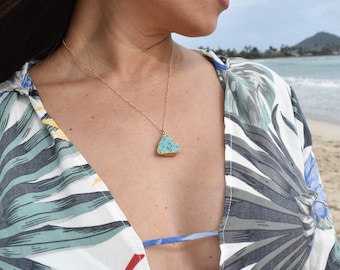 May include: A gold chain necklace with a turquoise triangle pendant. The pendant has a speckled pattern and is set against a white background.