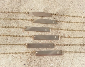 Op de afbeelding: Vijf gouden kettingen met een staafvormige hanger en initialen. De initialen zijn B, G, K, J en S.