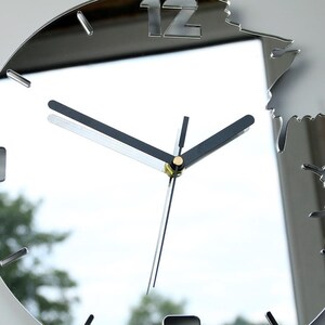 May include: A silver mirrored clock with black hands and Roman numeral markings. The clock face is surrounded by a decorative, irregular, mirrored frame.