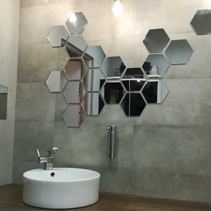Puede incluir: Un lavabo de ba&ntilde;o con un lavabo de porcelana blanca y un grifo cromado. La pared detr&aacute;s del lavabo est&aacute; decorada con un patr&oacute;n geom&eacute;trico de espejos hexagonales.