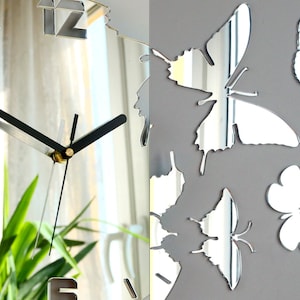 May include: A silver mirrored clock with black hands and Roman numeral markings. The clock is surrounded by silver mirrored butterflies.