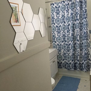 Puede incluir: Un ba&ntilde;o blanco con una cortina de ducha de patr&oacute;n azul y blanco, un lavabo y un tocador blancos, y un inodoro blanco. El ba&ntilde;o tiene un espejo hexagonal en la pared.