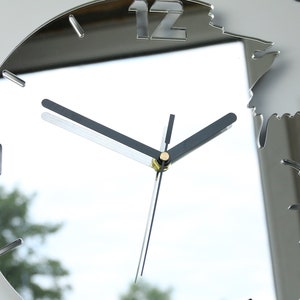 May include: A silver mirrored clock with black hands and a 12 at the top. The clock is designed to look like a broken mirror with a jagged edge.