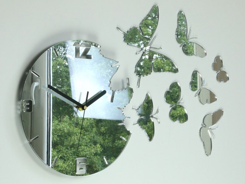 May include: A silver mirrored clock with a circular face and black hands. The clock is surrounded by several silver mirrored butterflies of varying sizes.