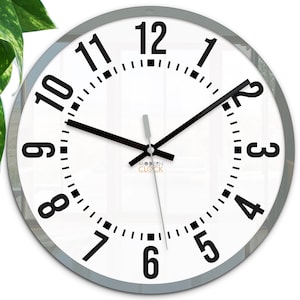 Op de afbeelding: Een witte ronde klok met zwarte cijfers en wijzers. De klok heeft een zilveren frame en is ingesteld op 1:30. De wijzerplaat van de klok heeft ook de tekst "MODERN CLOCK" erop gedrukt.