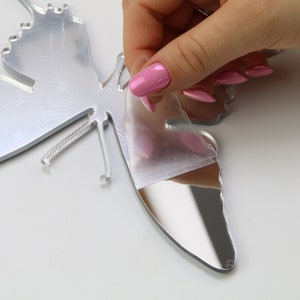 May include: A silver mirrored butterfly wall decor with a protective film being peeled off. The butterfly has a detailed design and is ready to be displayed.
