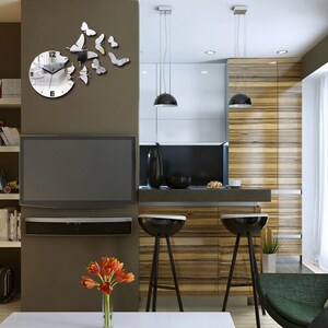 May include: A modern kitchen featuring a large flat screen television, a wooden worktop, and two bar stools. The wall behind the television has a mirrored clock with a butterfly design.