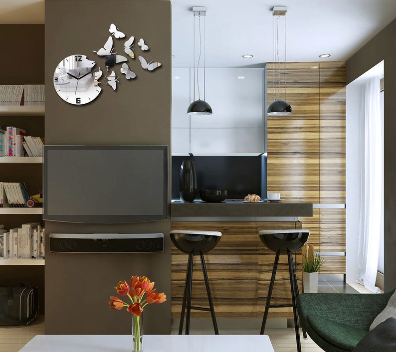 May include: A modern kitchen featuring a large flat screen television, a wooden worktop, and two bar stools. The wall behind the television has a mirrored clock with a butterfly design.