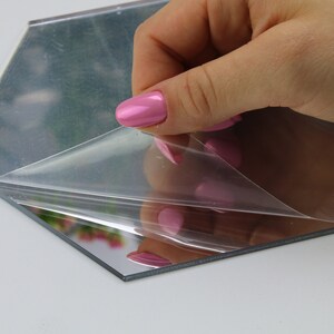 Puede incluir: Un espejo hexagonal con una pel&iacute;cula protectora que se est&aacute; despegando. El espejo tiene una superficie reflectante y est&aacute; rodeado por un marco de pl&aacute;stico transparente.