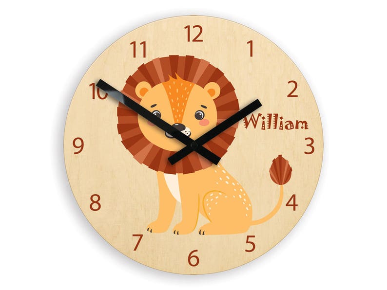 Puede incluir: Un reloj de madera con un dise&ntilde;o de le&oacute;n. La esfera del reloj tiene un le&oacute;n marr&oacute;n con una melena amarilla y una cola negra. La esfera del reloj tiene los n&uacute;meros del 1 al 12 y el nombre "William" est&aacute; escrito debajo del n&uacute;mero 3.