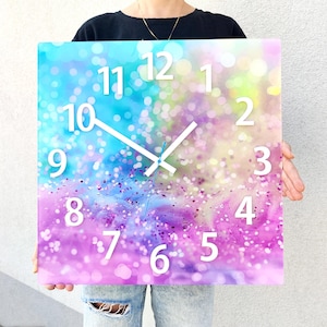 Puede incluir: Un reloj cuadrado con un fondo de purpurina arcoíris. La esfera del reloj tiene números y manecillas blancas. Los números son del 1 al 12.