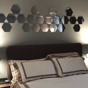 Puede incluir: Un dormitorio con una cama, dos l&aacute;mparas de noche y una pared decorada con un patr&oacute;n geom&eacute;trico de espejos hexagonales.